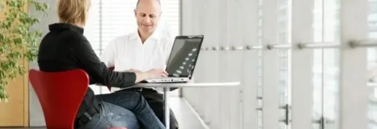 A man and a woman sitting at a table and the woman operating a laptop
